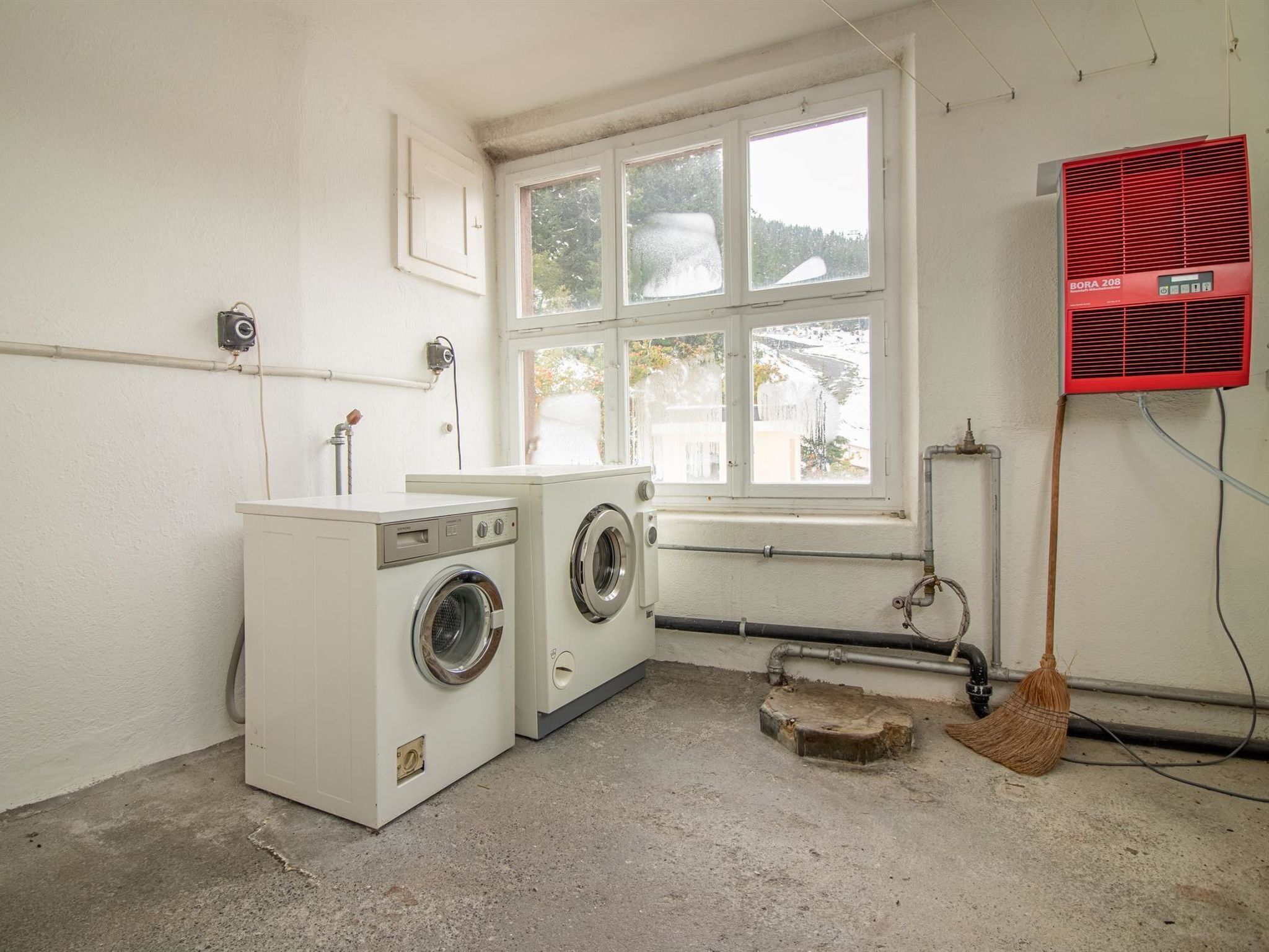 Une buanderie équipée d’un lave-linge, d’un sèche-linge, d’une fenêtre et d’un radiateur rouge.