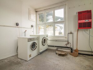 Ein Waschraum mit Waschmaschine, Trockner, einem Fenster und einem roten Heizgerät.