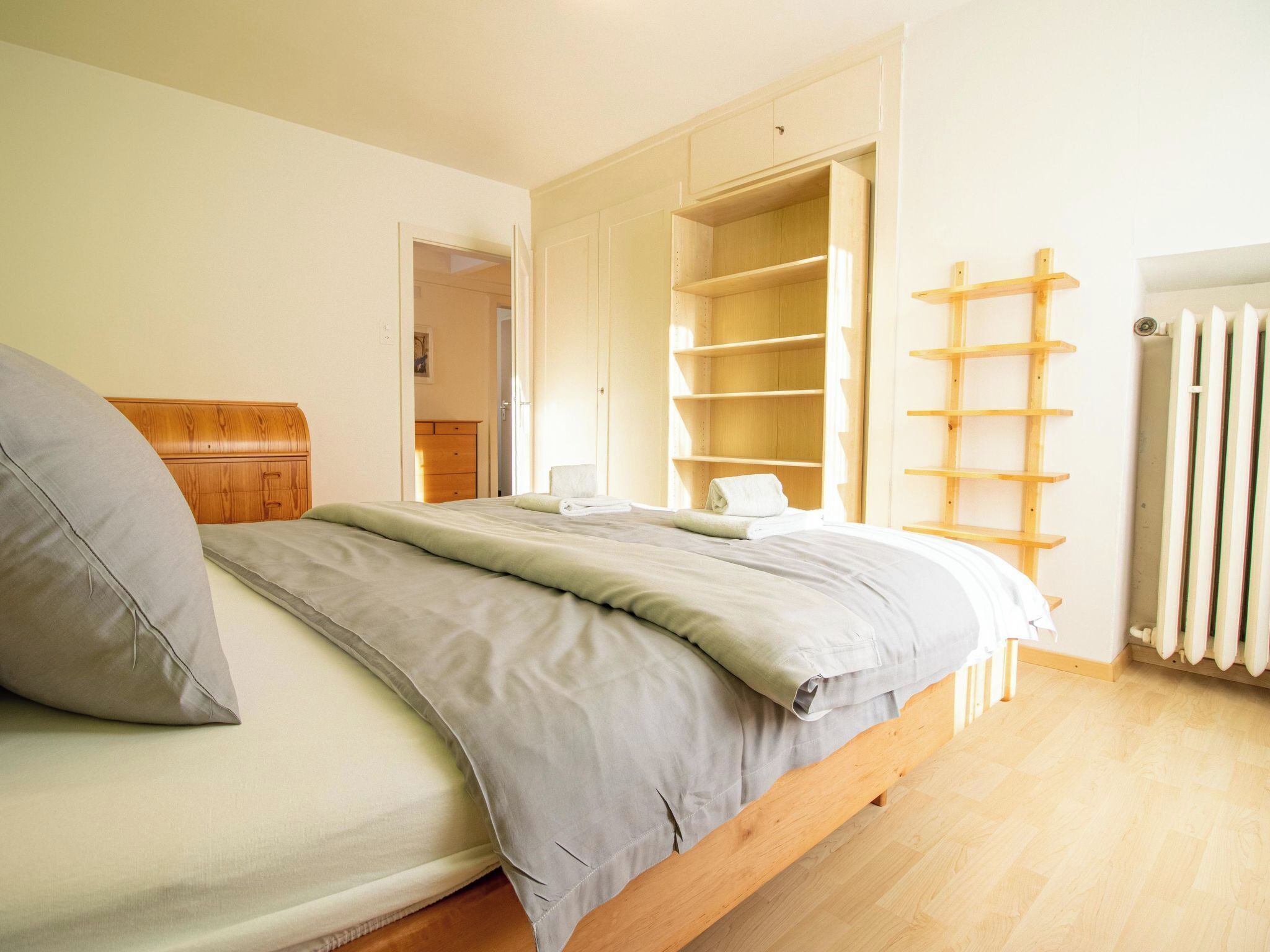 A bedroom with a bed, a wooden dresser, a wardrobe, and a radiator.