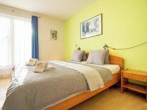 A single bed with a wooden frame, a bedside table, a wall-mounted lamp, and a window with blue curtains. - Haldahus 2 by Arosa Holiday Appartement/Fewo,  , 7-Bettwohnung Haldahus 2 by Interhome (Arosa)