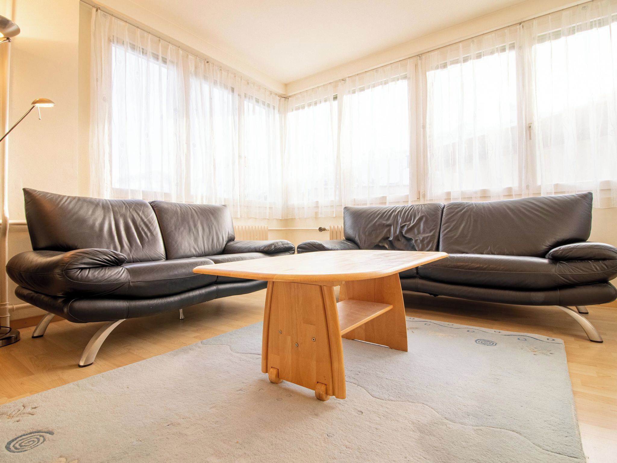 Una sala de estar moderna con un sofá de cuero, una mesa de centro de madera y cortinas translúcidas.