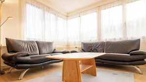 Una sala de estar moderna con un sofá de cuero, una mesa de centro de madera y cortinas translúcidas.