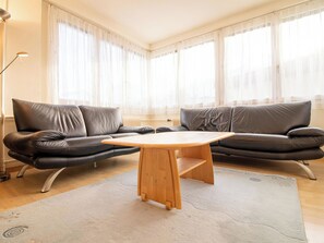 Ein stilvolles Wohnzimmer mit einem Ledersofa, einem Holztisch und transparenten Vorhängen.