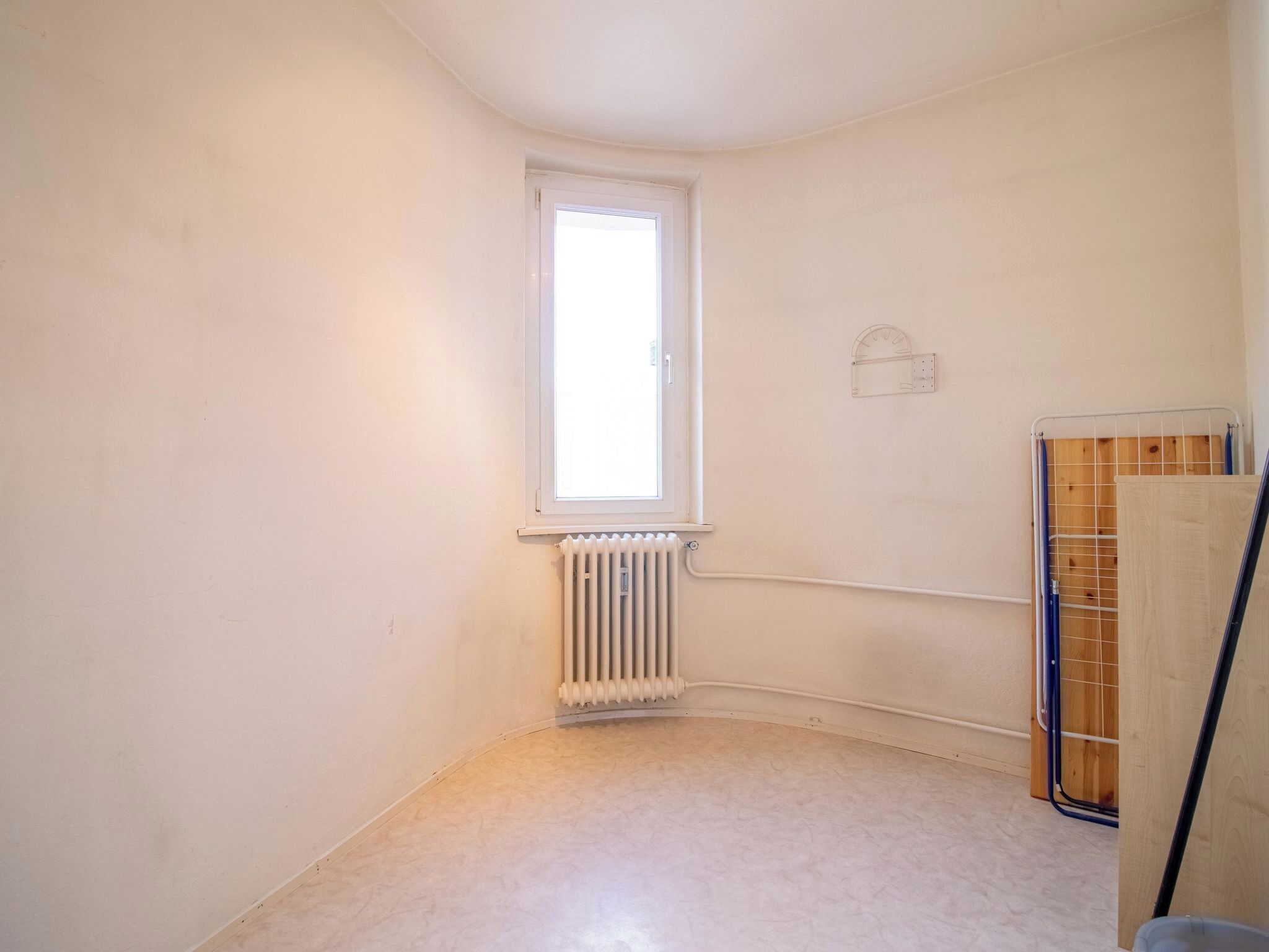A small, empty room with a window, radiator, and a metal rack.