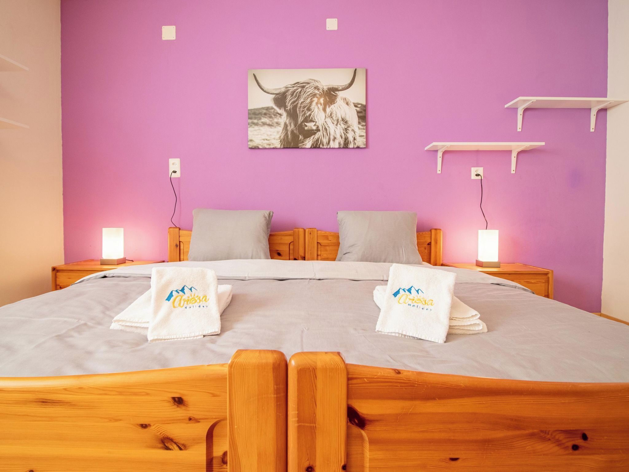 Une chambre à coucher comprenant un lit, deux tables de chevet, un tableau accroché au mur et des serviettes ornées d’un logo.