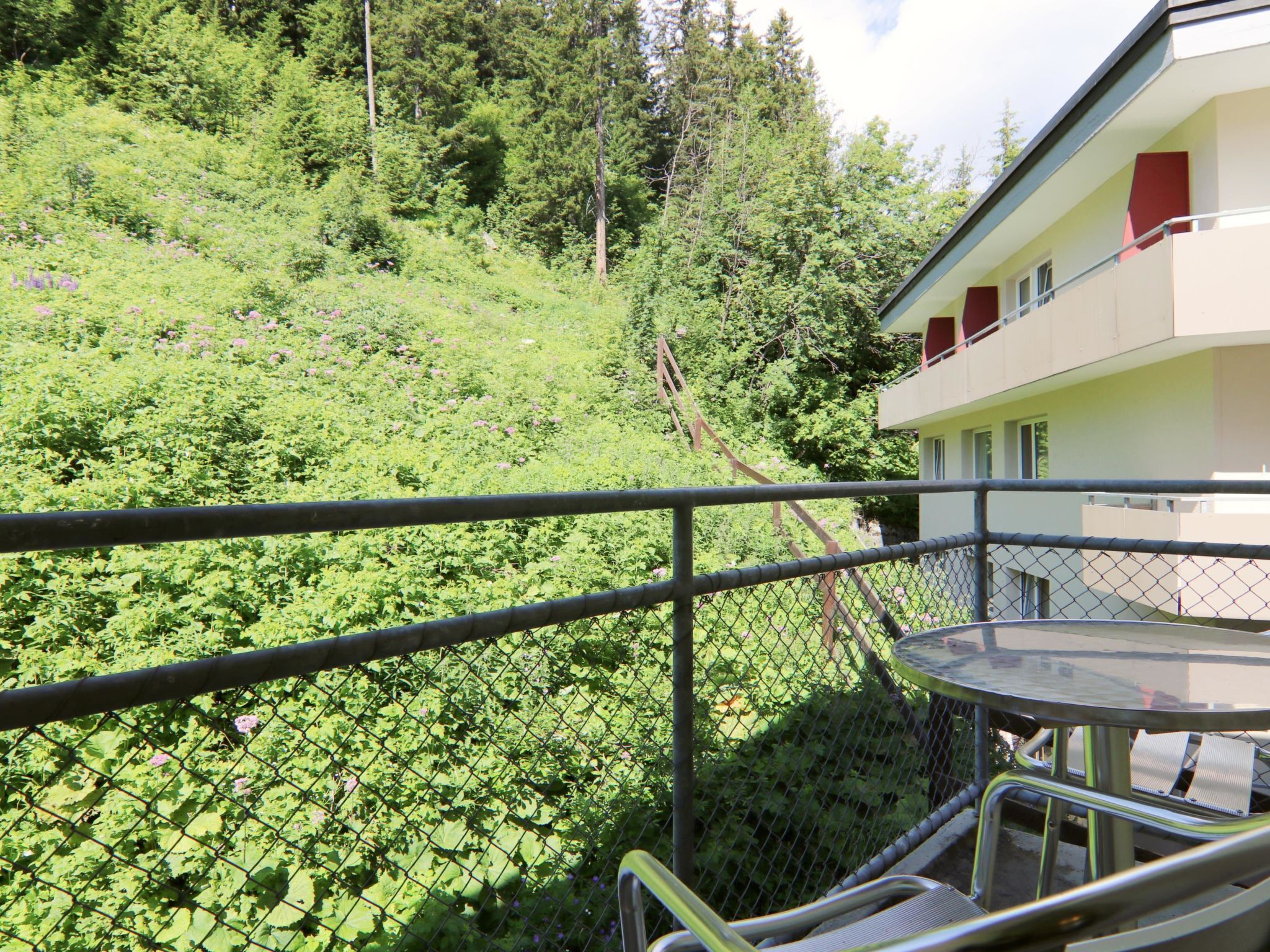 Un balcon doté d’une rambarde en métal, donnant sur une colline verdoyante.