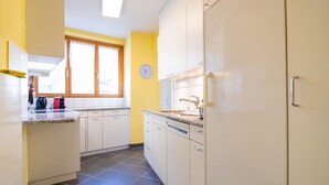 Una cocina con armarios blancos, lavavajillas y ventana con un reloj.