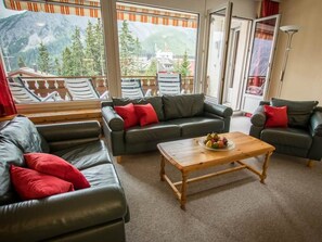 A living room with leather sofas, a wooden coffee table, and a mountain view through large windows. - Chalchboda 1 Appartement/Fewo, Bad, WC, 6-Bettwohnung by Interhome (Arosa)