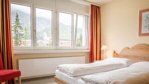 Habitación de hotel con dos camas, una ventana con cortinas, una silla roja y una lámpara sobre una mesita de noche.