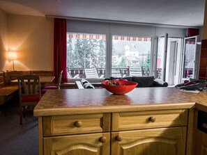 A hotel room with a wooden counter, a bowl of fruit, a sofa, and a view of the outside. - Chalchboda 1 Appartement/Fewo,  , 6-Bettwohnung by Interhome (Arosa)