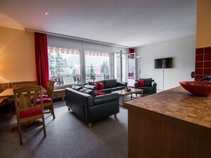 A modern living room with a sofa, a dining table, and a large window. - Chalchboda 1 Appartement/Fewo, Bad, WC, 6-Bettwohnung by Interhome (Arosa)