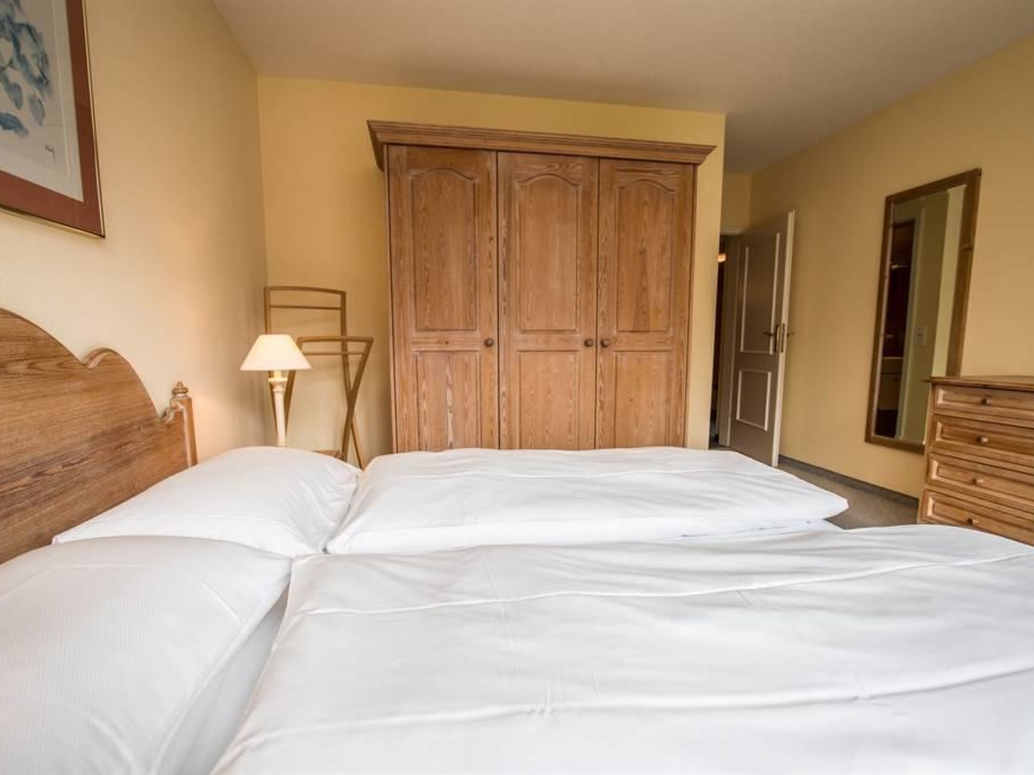 A hotel room with a double bed, wooden wardrobe, and a nightstand with a lamp.