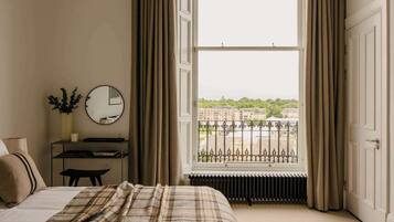 A bedroom with a bed, a bedside table, a mirror, and a window with a view of buildings.