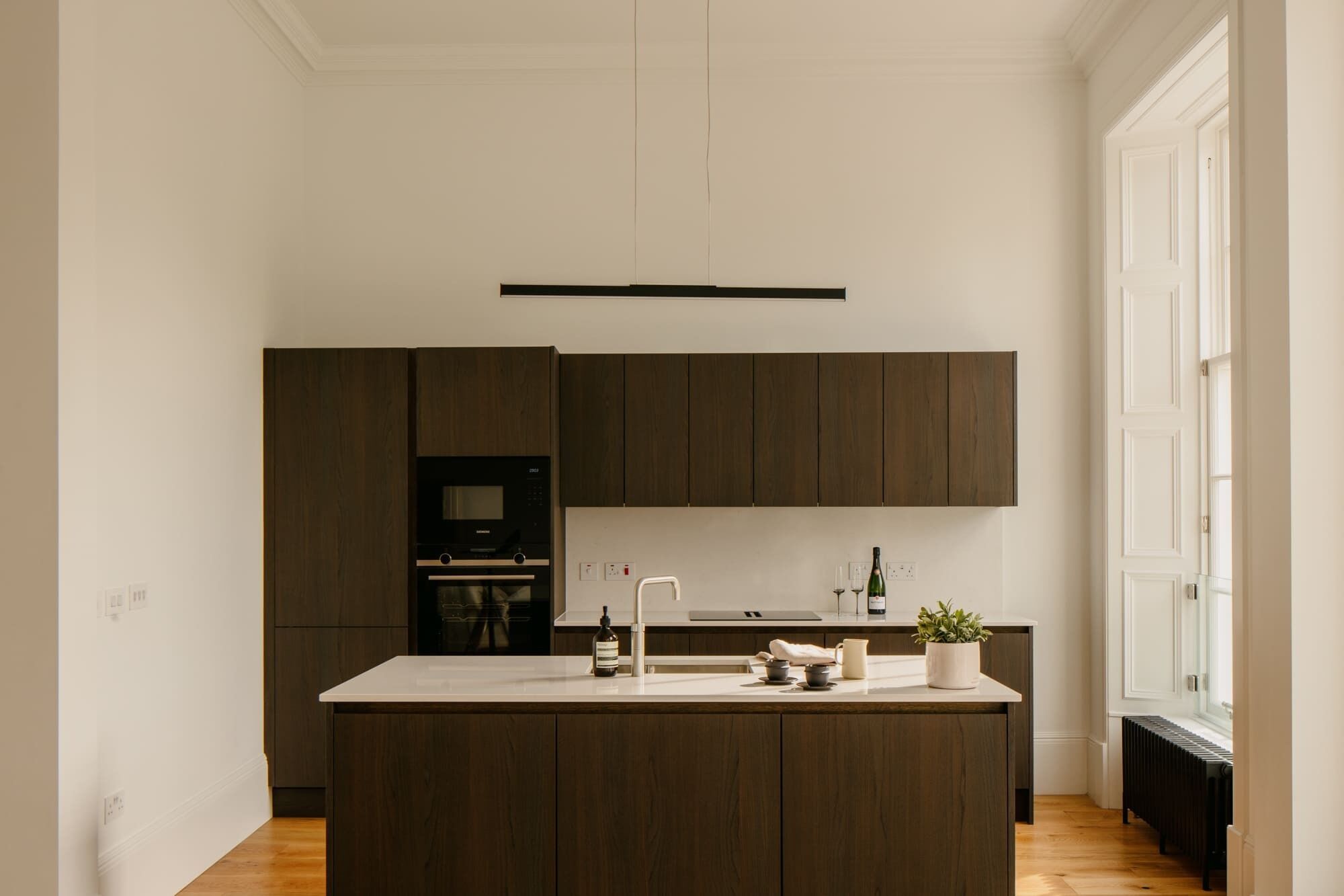 A modern kitchen with dark wood cabinets, a central island, and a built-in oven.
