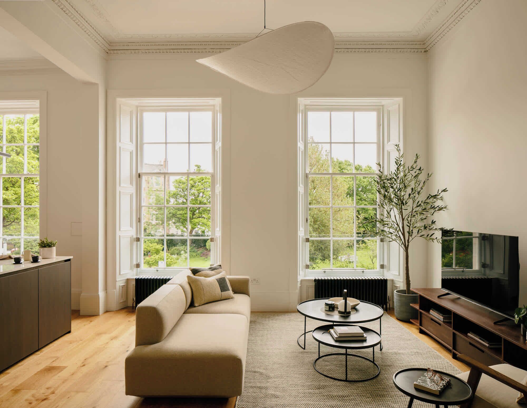 A modern living room with a sofa, coffee table, TV, and large windows.
