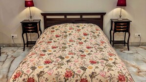 Un letto con copriletto floreale, due comodini con lampade e un pavimento in marmo.