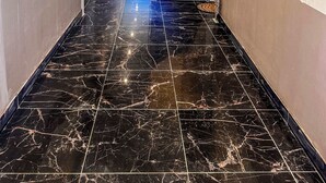 Un corridoio con pavimento in marmo, una scala e una porta in fondo.