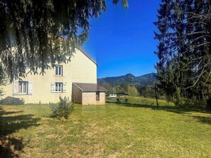 Ein zweistöckiges Haus mit Ziegelanbau, umgeben von einem Rasen und Bäumen.