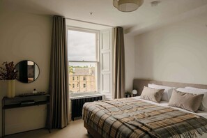 Ein Schlafzimmer mit Bett, Nachttisch, Heizkörper, einem fenster mit Vorhängen und einem Spiegel an der Wand.