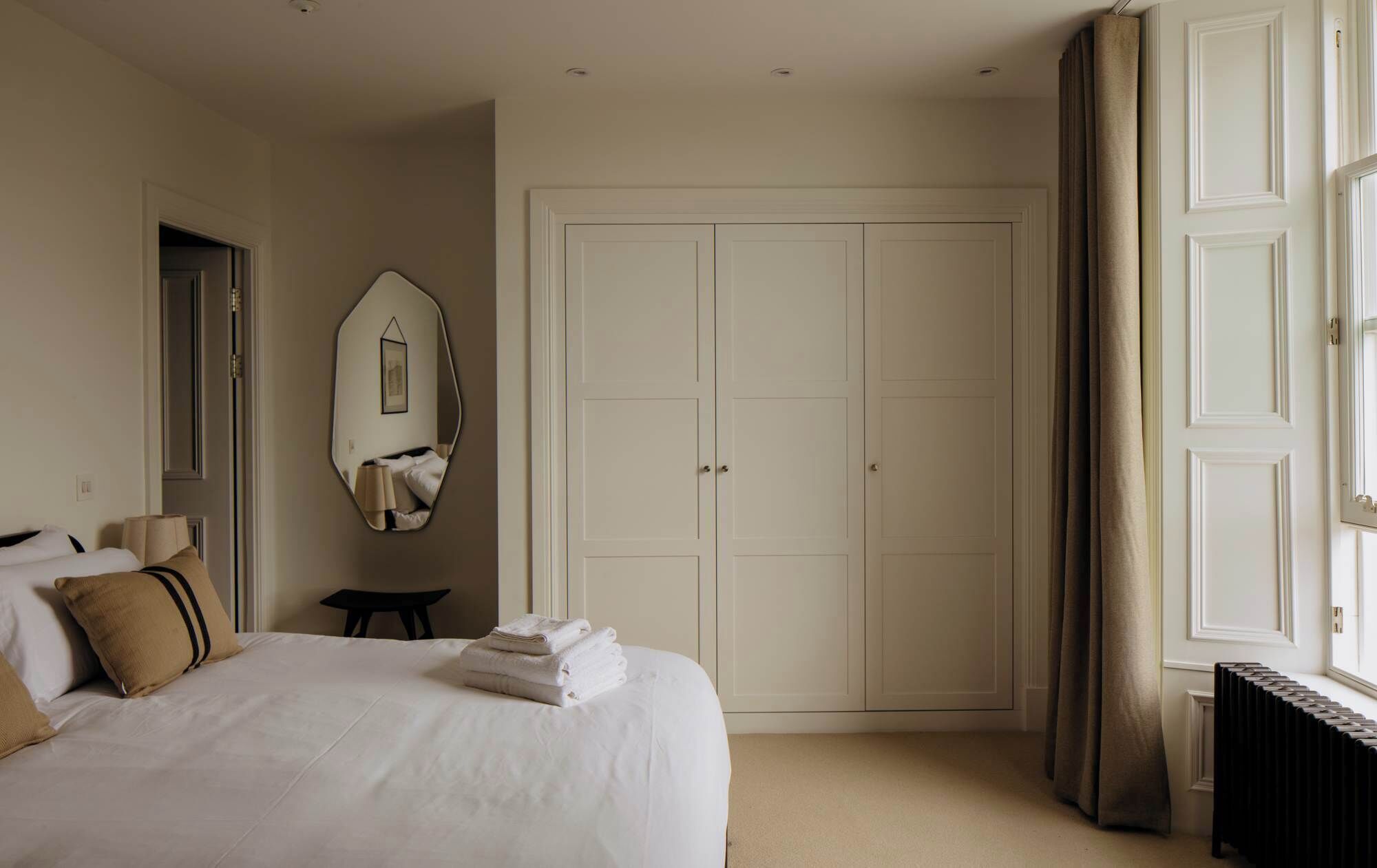 Una habitación de hotel con cama, espejo, armario y ventana con cortinas.