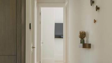 A hallway with a wooden wardrobe, a radiator, a small stool, and a wall-mounted shelf with a plant.