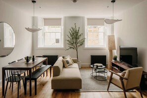 Ein modernes Wohnzimmer mit einer Couch, einem Esstisch, Stühlen, einem Fernseher und einem großen Fenster.
