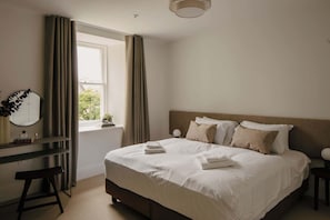 A bedroom with a bed, bedside tables, a desk, a mirror, and a window with curtains. - Inviting Apartment in Claremont Residences (Edinburgh)