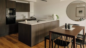 Et moderne køkken med en central ø, mørke skabe, et spiseområde med bord og stole, og et rundt spejl på væggen.