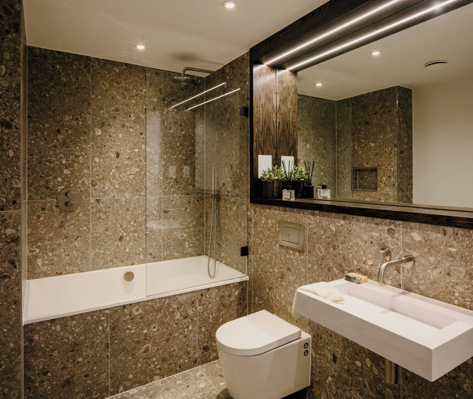 A modern bathroom with a glass-enclosed shower, a white toilet, and a white sink with a mirror above.