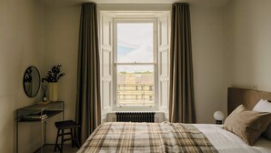 Un dormitorio con cama, escritorio, silla, radiador y ventana con cortinas.