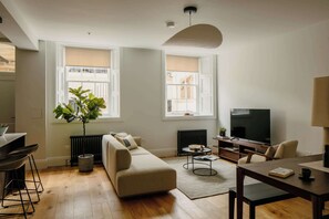 A modern living room with a sofa, a dining table, a TV, and a large window. - Charming Apartment in Claremont Residences (Edinburgh)