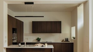 Una cocina moderna con armarios de madera oscura, encimera blanca y dos taburetes de bar.