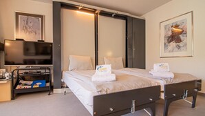 A hotel room with two beds, a desk with a computer, a TV, and artwork on the walls. - Rothornblick 39 by Arosa Holiday Appartement/Fewo,   4-Bettwohnung by Interhome (Arosa)