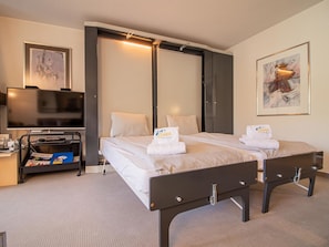 Ein Hotelzimmer mit zwei Betten, einem Schreibtisch mit Computer, einem Fernseher und Bildern an der Wand.