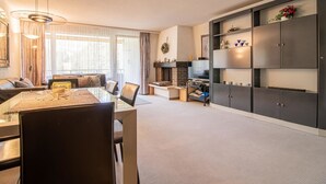 A modern living room with a dining area, a fireplace, and a large cabinet with shelves. - Rothornblick 39 by Arosa Holiday Appartement/Fewo,   4-Bettwohnung by Interhome (Arosa)