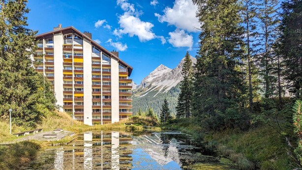 A multi-story hotel with balconies, a reflection pool, and a mountain backdrop. - Rothornblick 39 by Arosa Holiday Appartement/Fewo,   4-Bettwohnung by Interhome (Arosa)