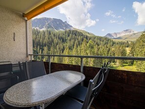 A balcony with a table and chairs, overlooking a forested mountain range.