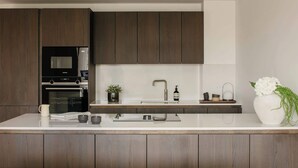 Een moderne keuken met donkerhouten kastjes, een wit aanrecht, een ingebouwde oven, een magnetron, een spoelbak met een moderne kraan, en een vaas met bloemen.