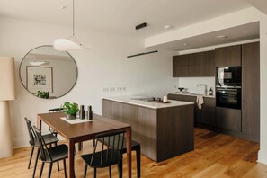 A modern kitchen with a central island, wooden flooring, and dark cabinetry. - Stylish Apartment in Claremont Residences (Edinburgh)