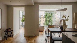 Een modern interieur met een eethoek, een groot raam met uitzicht op gebouwen en bomen, en een hanglamp.
