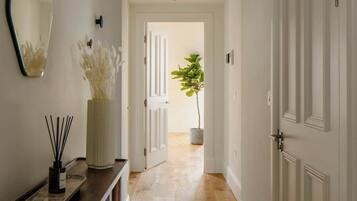 A hallway with wooden flooring, white doors, a mirror, a vase with dried flowers, and a potted plant.