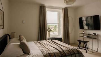 A bedroom with a bed, a desk, a TV, and a window with curtains.