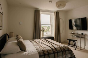 Ein Schlafzimmer mit einem Bett, einem Schreibtisch, einem Fernseher und einem Fenster mit Vorhängen.