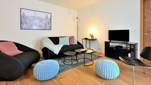 Un salon moderne avec un canapé, des poufs, une table basse, un meuble pour la télévision et un tableau encadré au mur.