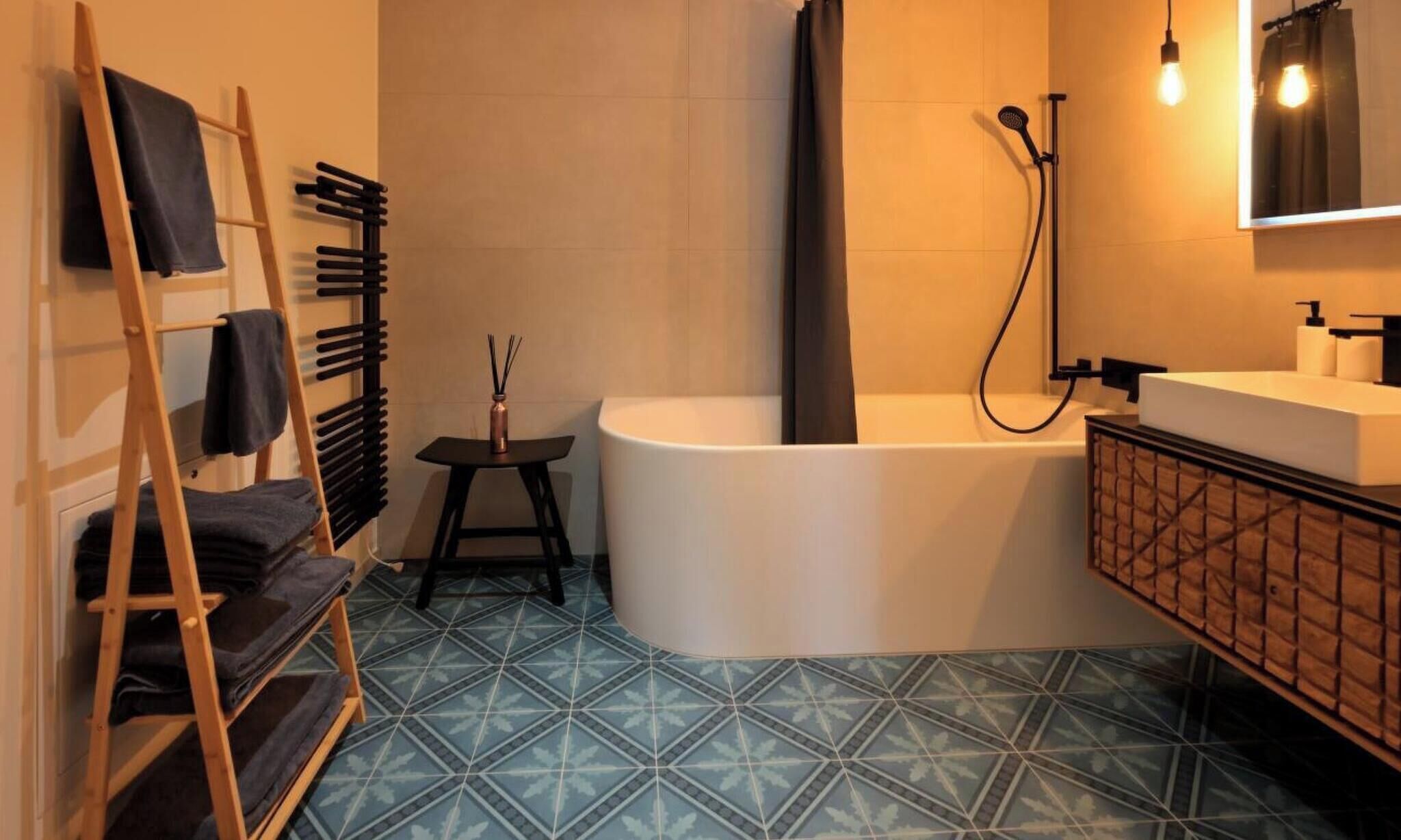 Ein Badezimmer mit einer Badewanne, einer Holzleiter, einem kleinen Tisch mit einer Flasche und einem Spiegel mit Beleuchtung.