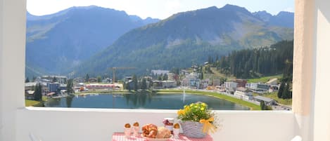 A balcony with a table set for breakfast overlooking a lake and mountains.