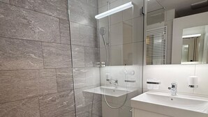 Une salle de bain moderne avec une douche à parois de verre, un meuble-lavabo blanc avec un miroir et un sol carrelé.