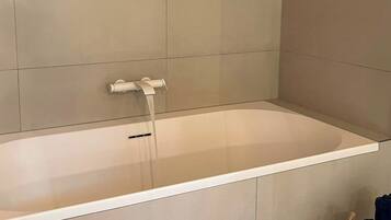 Un baño moderno con una bañera grande, vigas de madera en el techo y una paleta de colores neutros.