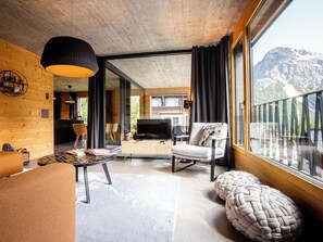 Un intérieur moderne avec un plafond en bois, un coin repas, un téléviseur et une grande fenêtre donnant sur la montagne.