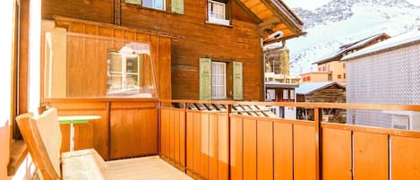 A wooden chalet with a balcony, a bench, and a view of snow-covered mountains.